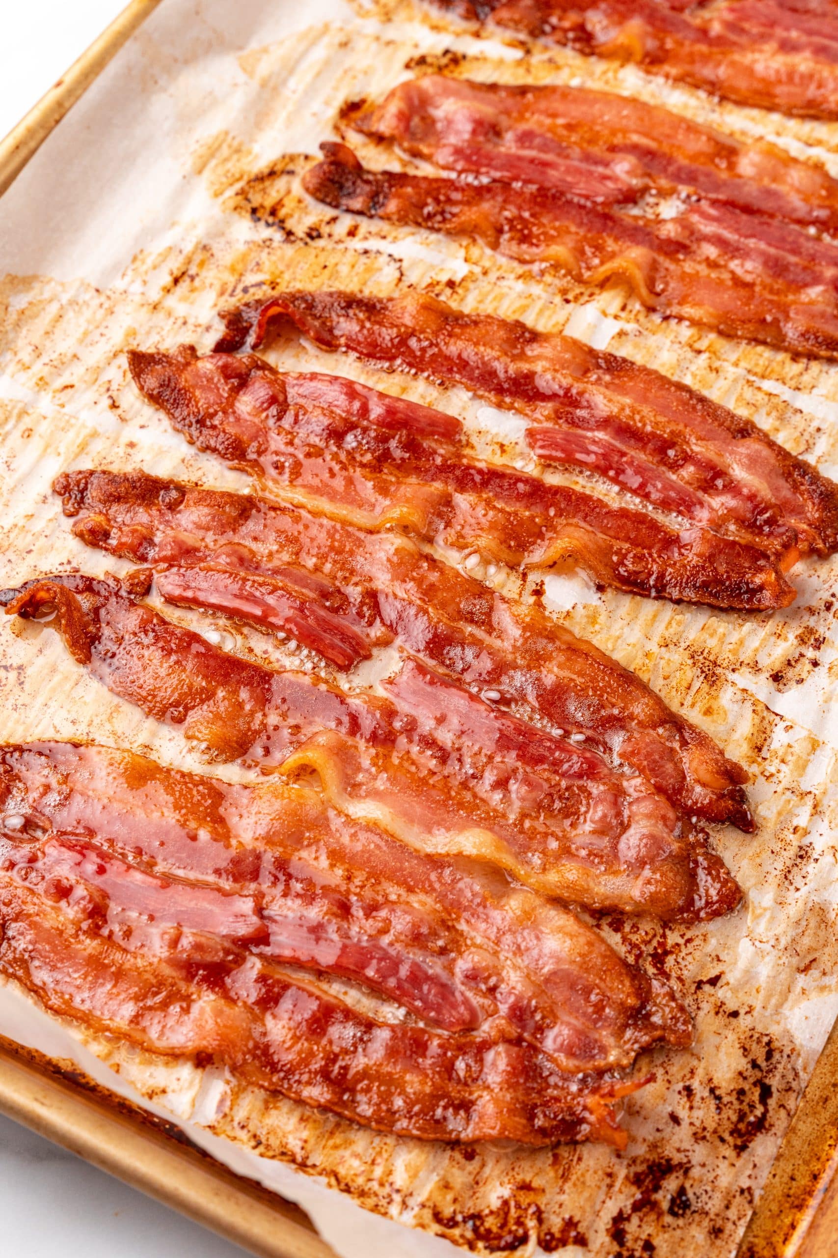 slices of baked crispy bacon in the oven on a parchment paper lined sheet pan