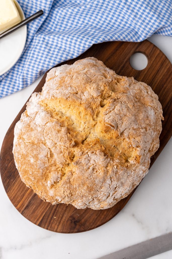 a golden brown baked loaf of traditional irish soda bread on a wooden cutting board