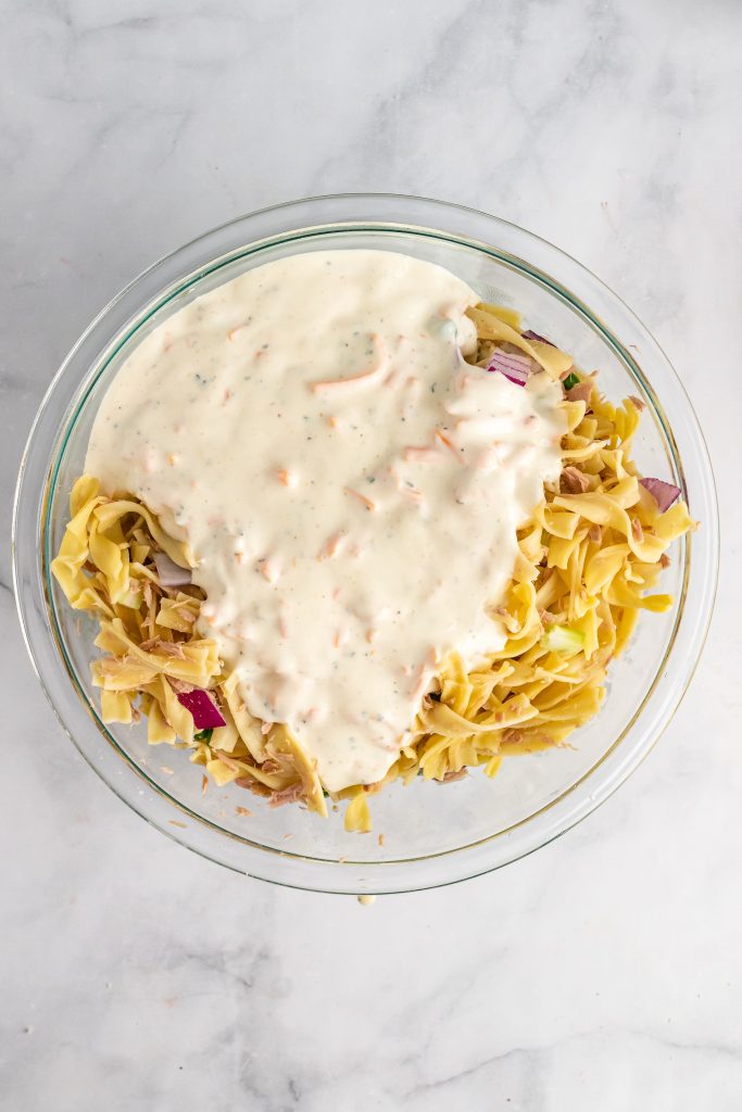 creamy tuna noodle casserole white sauce poured over pasta in a glass mixing bowl