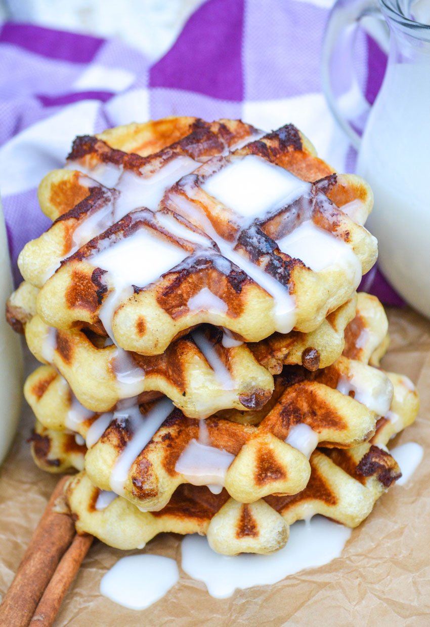a stack of cinnamon roll waffles dripping with a white cream cheese glaze