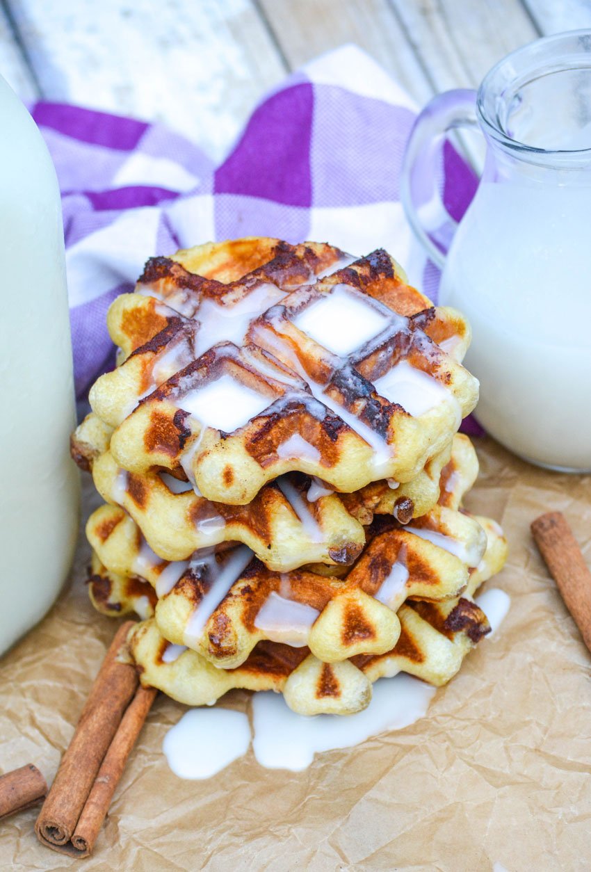 a stack of cinnamon roll waffles dripping with a white cream cheese glaze