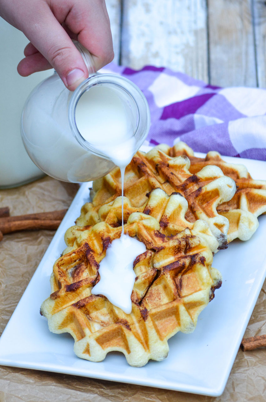 a thin cream cheese glaze being poured over a row of cinnamon roll waffles