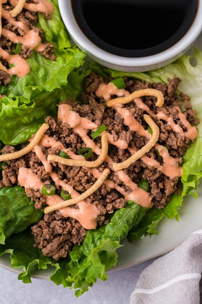 sriracha beef lettuce wraps drizzled with sauce and served on a white plate with a cup of soy sauce