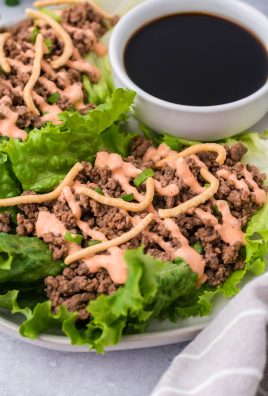 sriracha beef lettuce wraps drizzled with sauce and served on a white plate with a cup of soy sauce