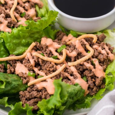 sriracha beef lettuce wraps drizzled with sauce and served on a white plate with a cup of soy sauce