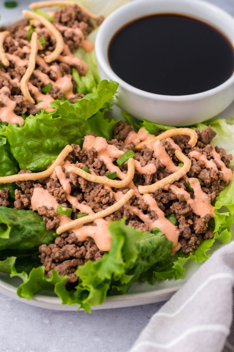 sriracha beef lettuce wraps drizzled with sauce and served on a white plate with a cup of soy sauce