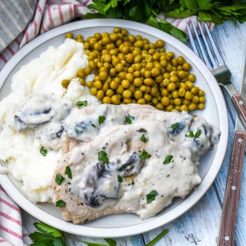herbed pork chops in mushroom gravy over mashed potatoes with peas on the side on a white plate