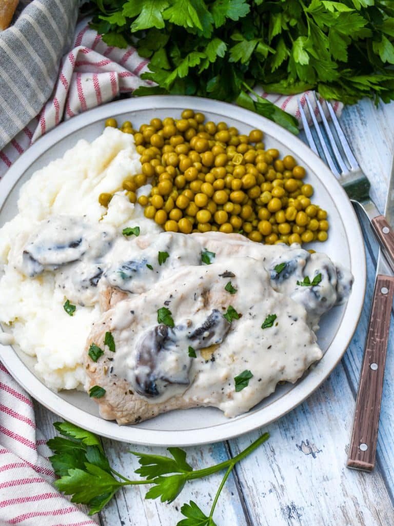 herbed pork chops in mushroom gravy over mashed potatoes with peas on the side on a white plate