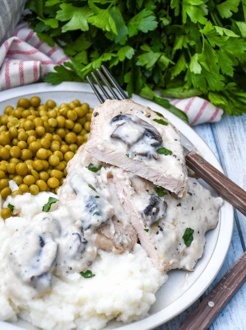 herbed pork chops in mushroom gravy over mashed potatoes with peas on the side on a white plate