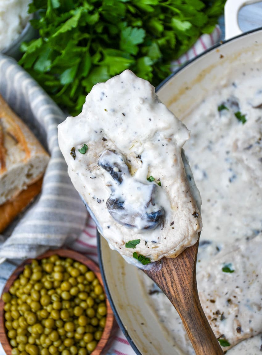 a wooden spatula holding up a pork chop in creamy mushroom gravy