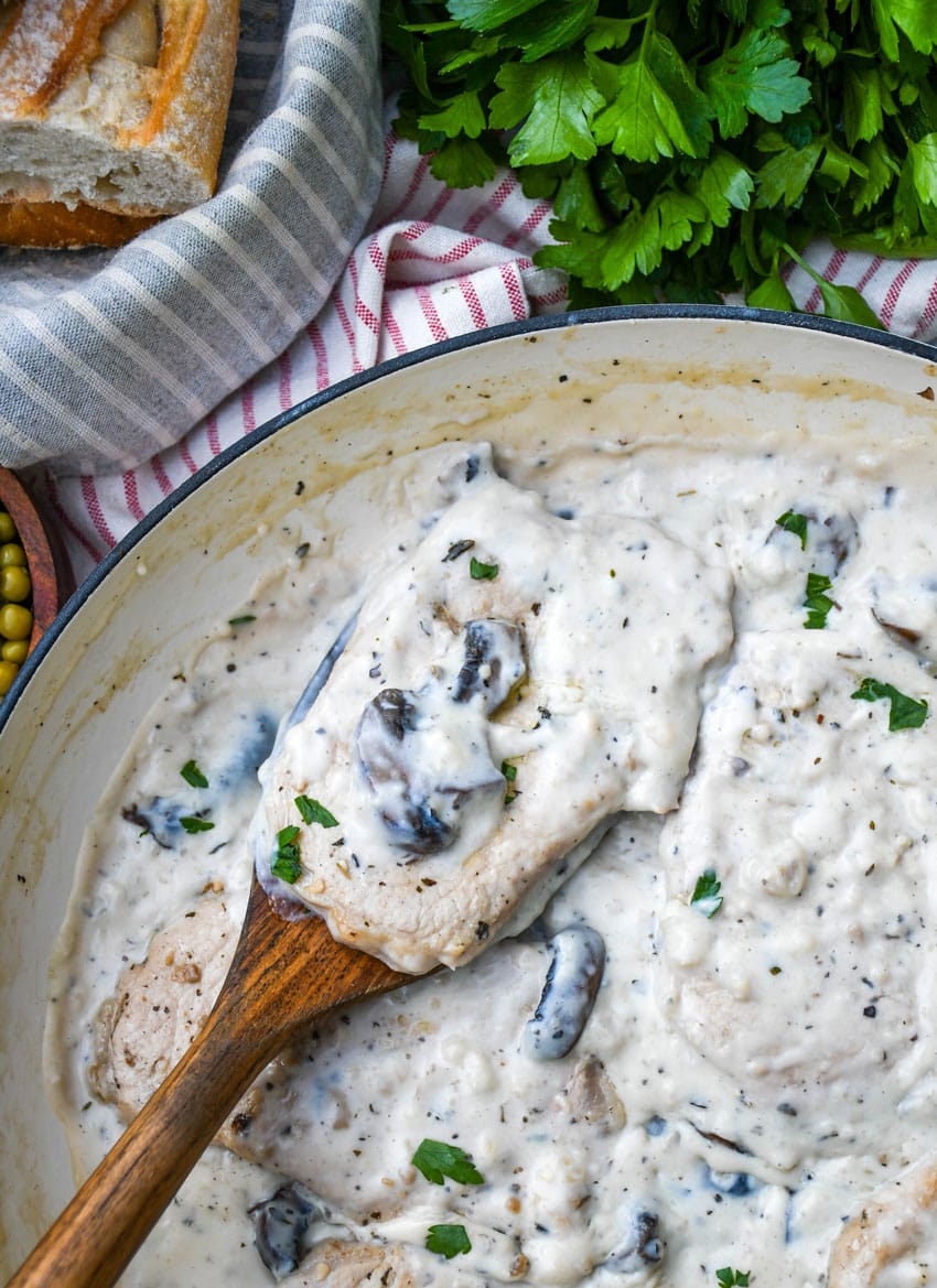 a wooden spatula lifting a pork chop in mushroom gravy out of a large cast iron skillet
