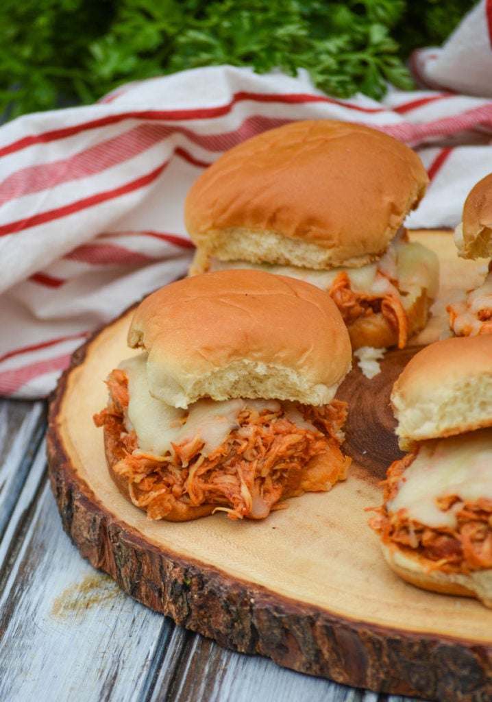 four crockpot chicken parmesan sliders on a wooden cutting board