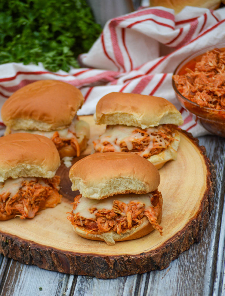 four crockpot chicken parmesan sliders on a wooden cutting board