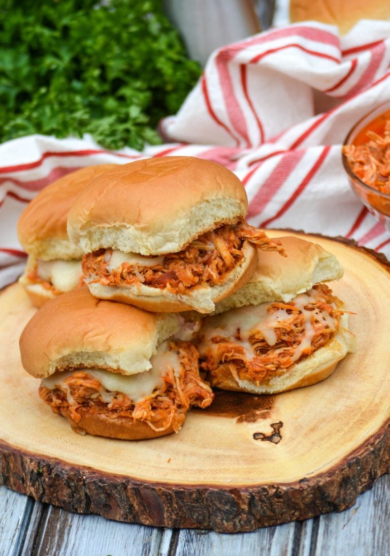 three crockpot chicken parmesan sliders stacked on a wooden cutting board