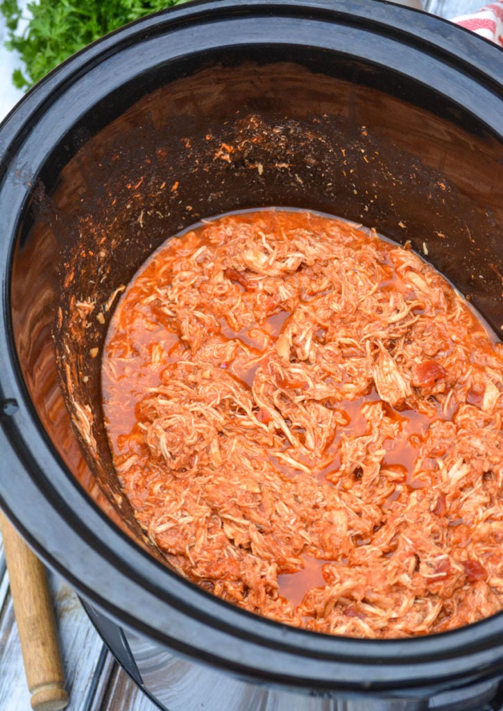sauced shredded chicken shown in the black bowl of a crockpot