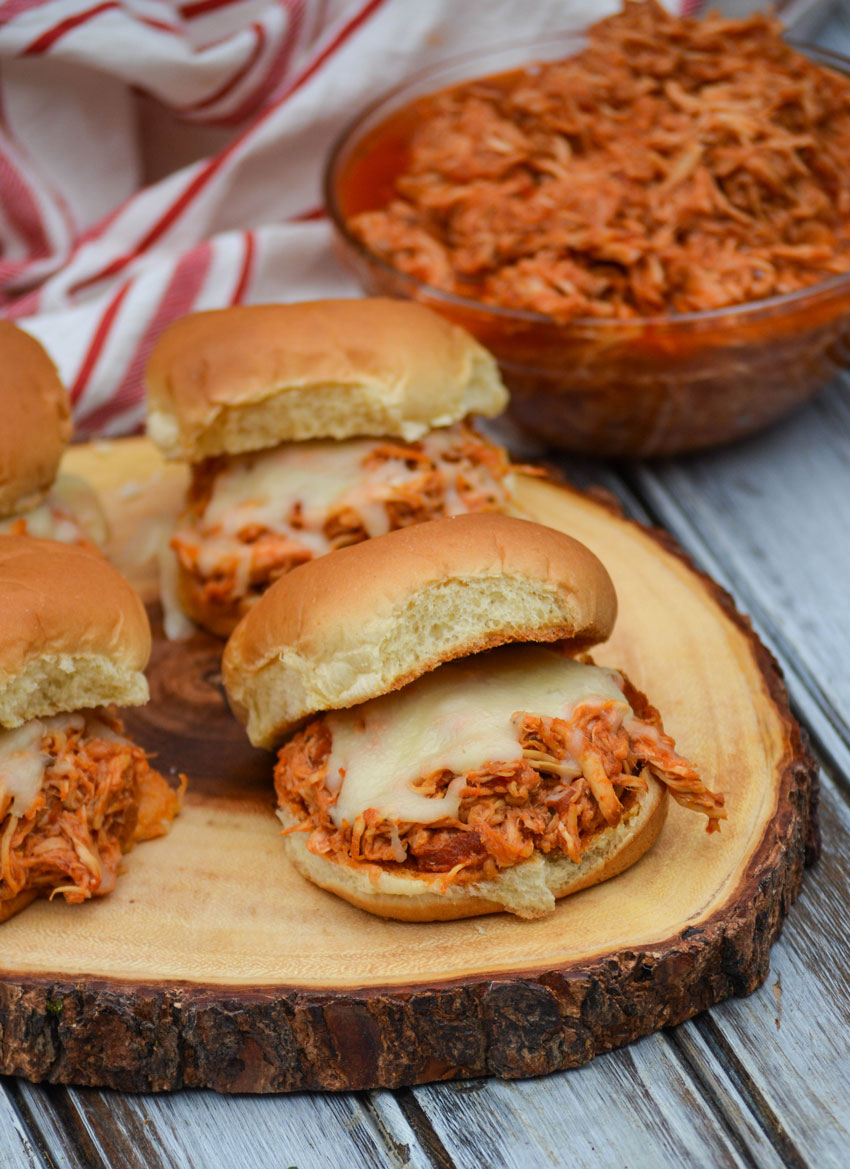 four crockpot chicken parmesan sliders on a wooden cutting board