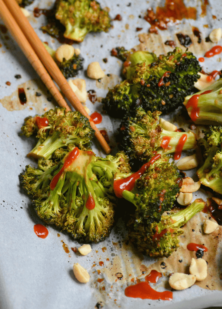 baked sriracha broccoli on white parchment paper with a pair of light brown chop stix