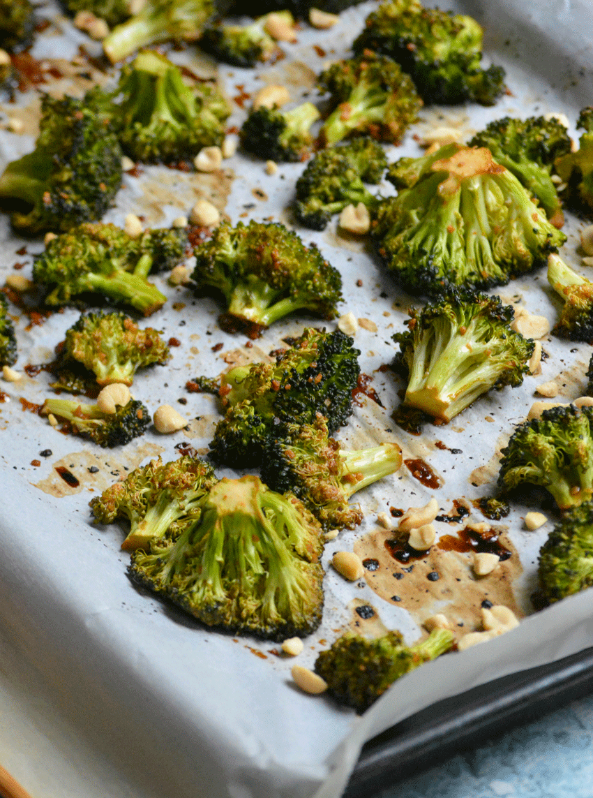 baked broccoli and crushed peanuts shown on a white parchment paper lined sheet pan