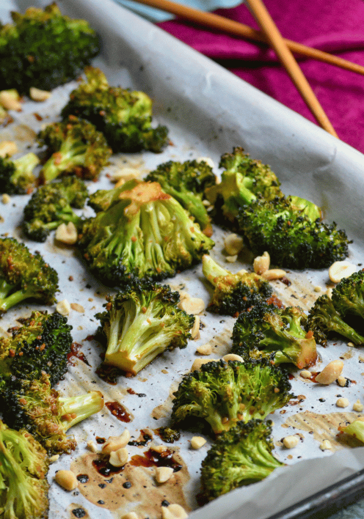 baked broccoli and crushed peanuts shown on a white parchment paper lined sheet pan