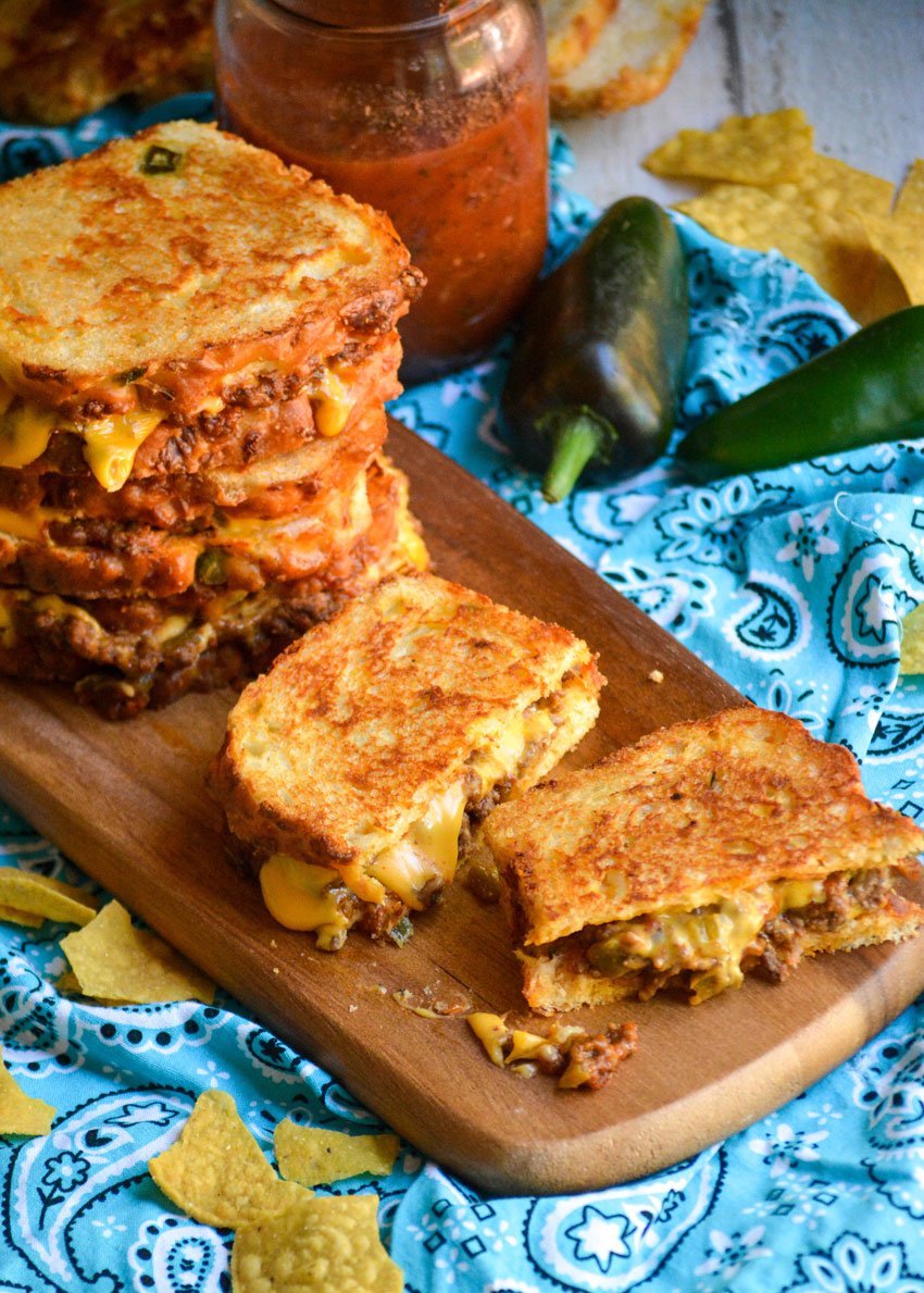 a sliced grilled cheese sandwich with ground beef on a wooden cutting board