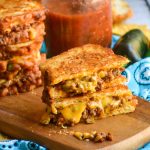 two halves of a cheesyTex Mex grilled cheese stacked together on a wooden cutting board