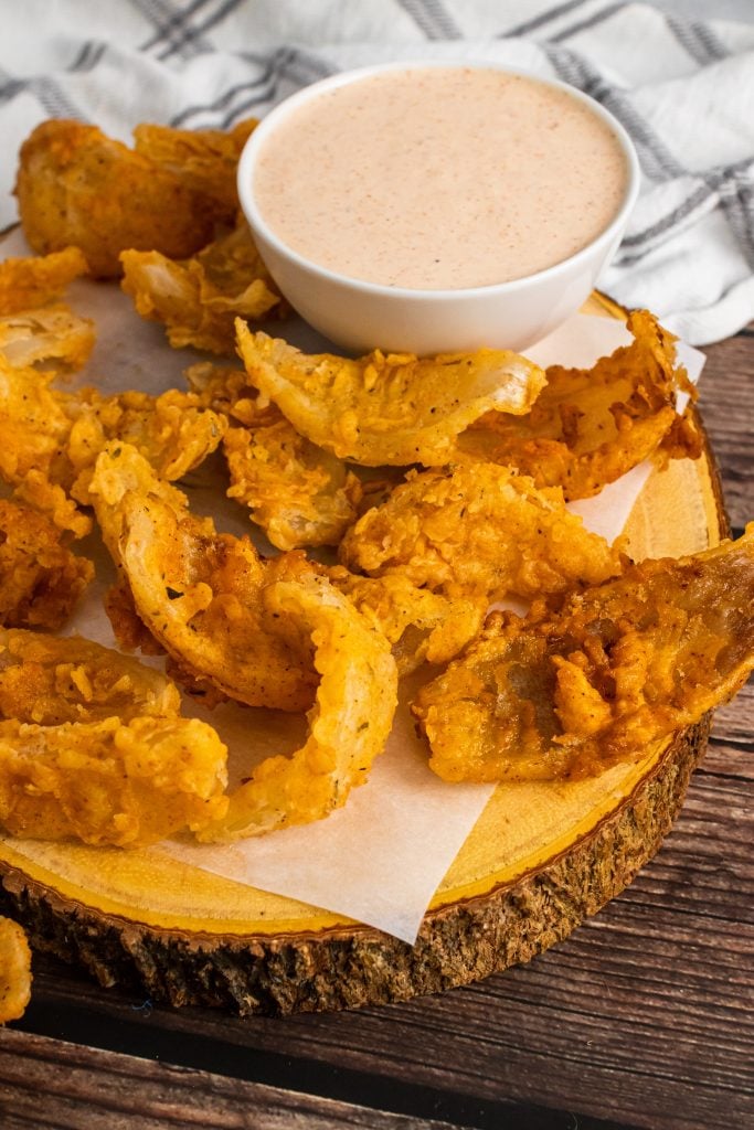 bloomin onion bites on a parchment paper covered cutting board with a white bowl filled with dipping sauce