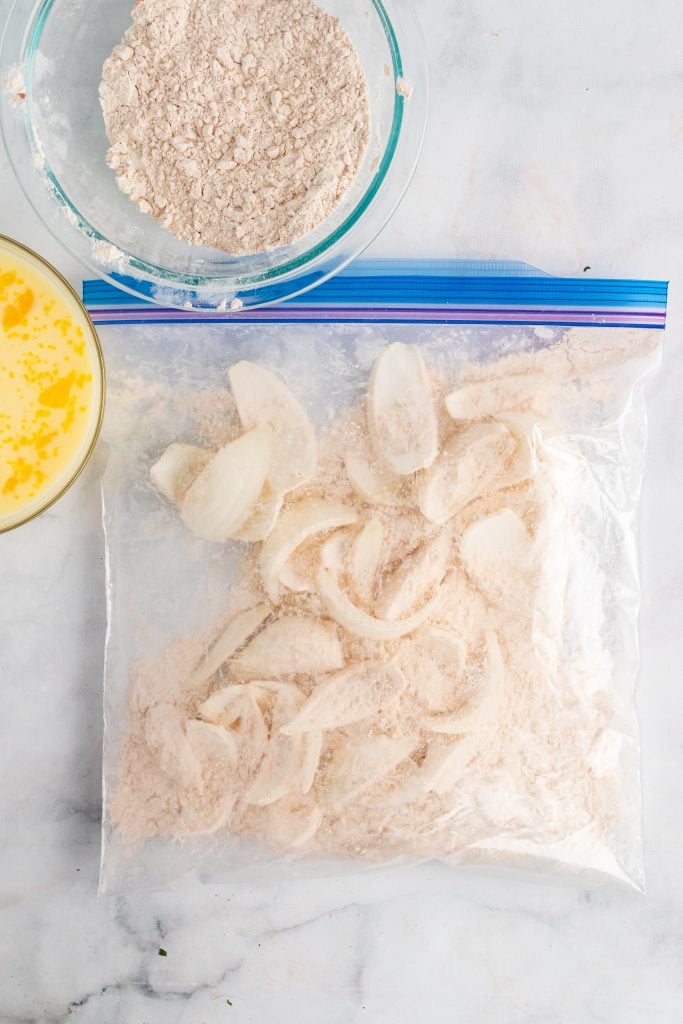 onion petals coated in flour in a large ziplocking bag laid out flat on a marbled countertop