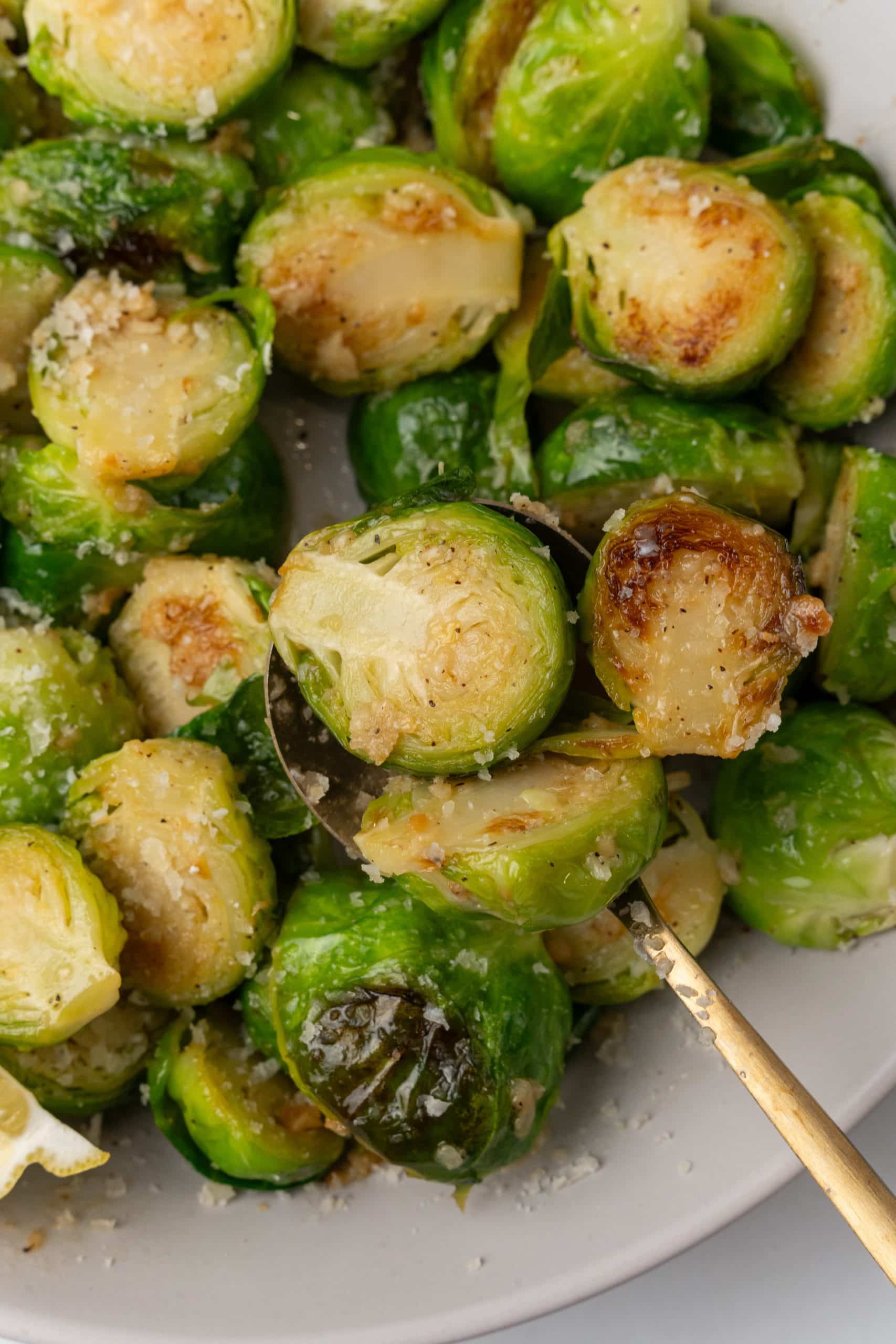 a gold spoon scooping sauteed brussels sprouts with lemon and garlic out of a white bowl