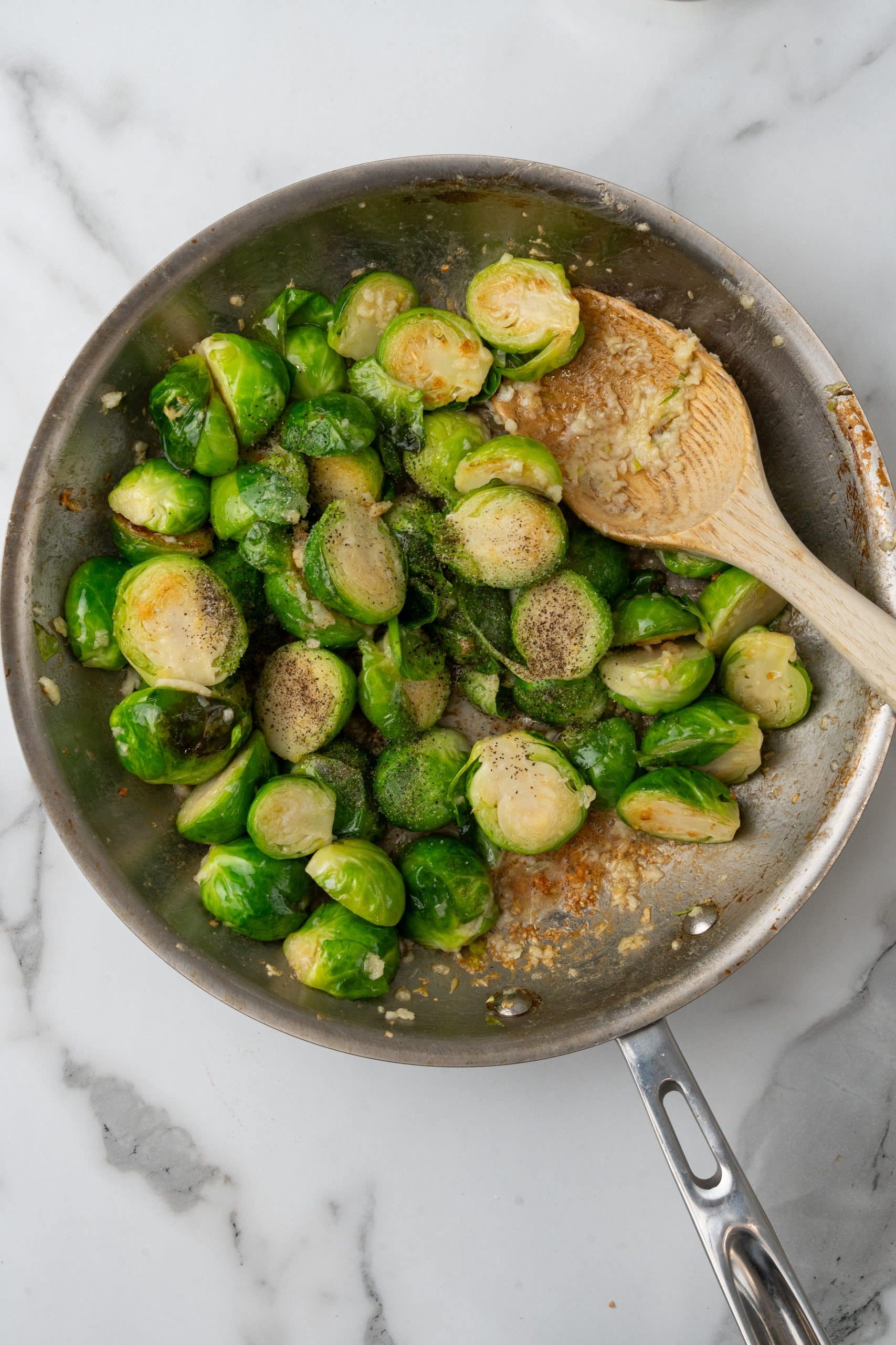 sauteed brussels sprouts in a silver sauce pan with garlic and lemon with a wooden spoon resting on the edge