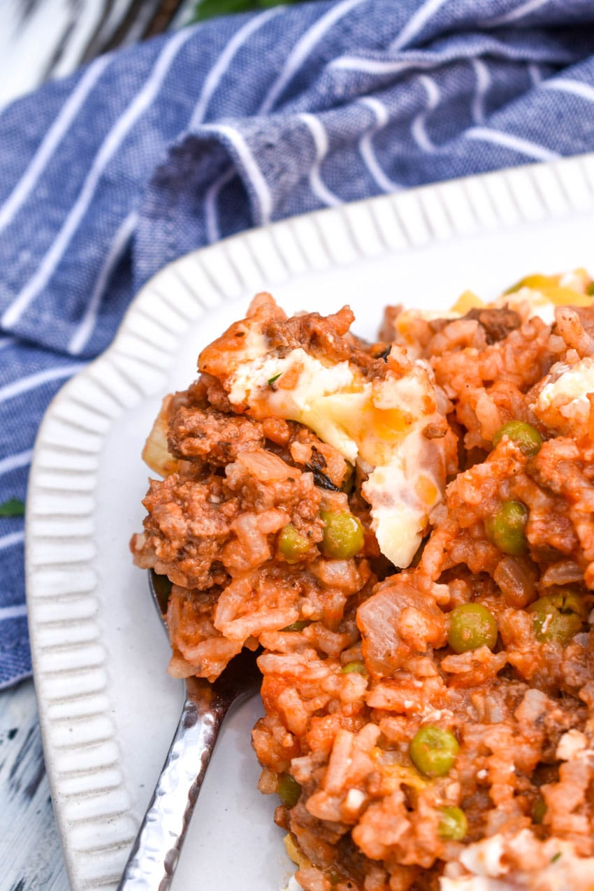 a silver fork resting on the edge of a white plate filled with cheesy ground beef and rice casserole