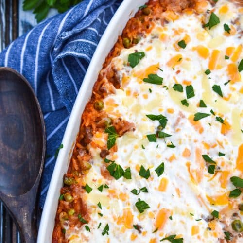 cheesy ground beef and rice casserole in a white baking dish with a wooden spoon on the side