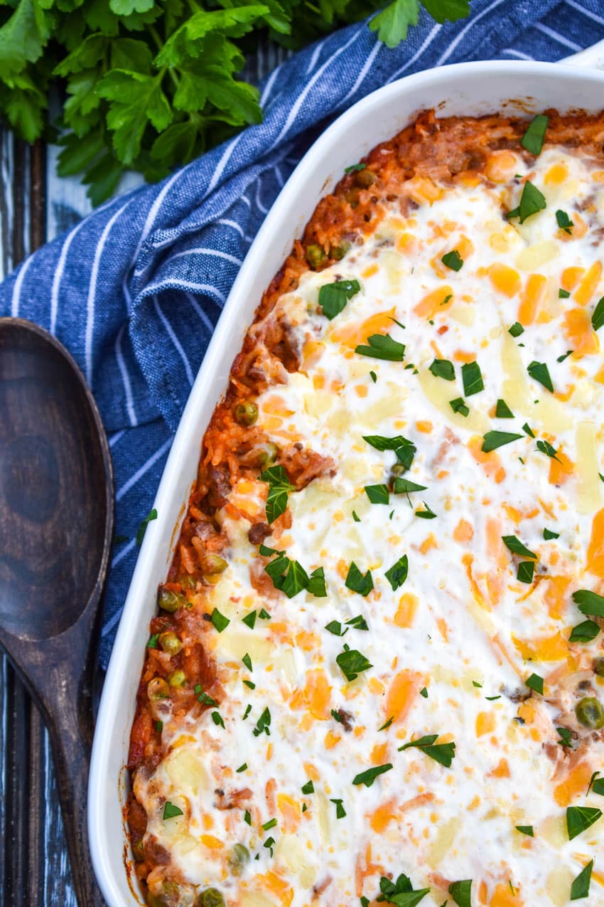 cheesy ground beef and rice casserole in a white baking dish with a wooden spoon on the side