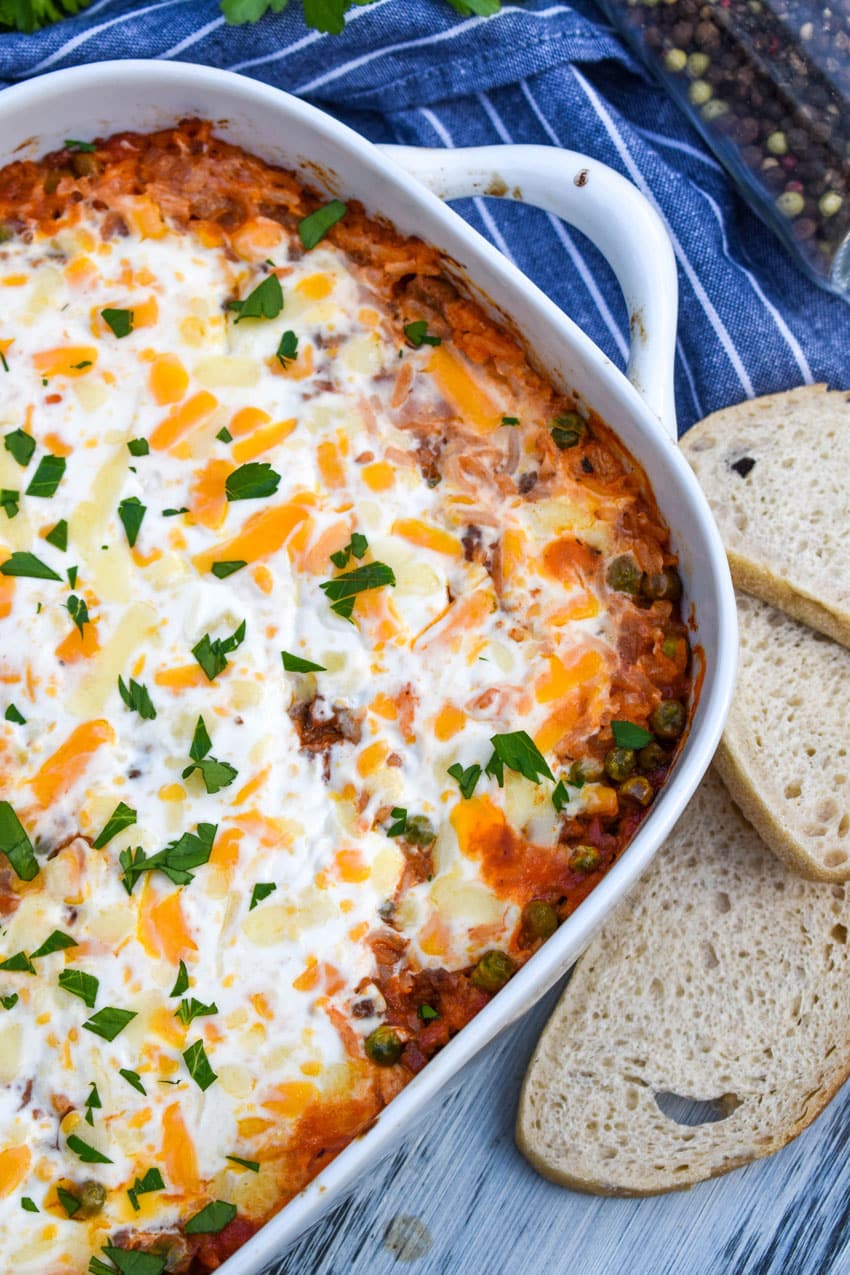 cheesy ground beef and rice casserole in a white baking dish with a wooden spoon on the side