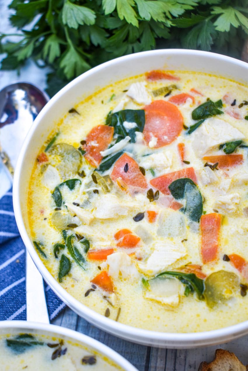 chicken florentine soup in a white bowl with fresh herbs and slices of bread on the side