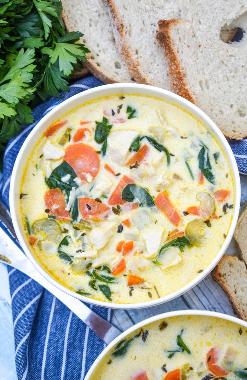 chicken florentine soup in a white bowl with fresh herbs and slices of bread on the side