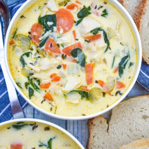 chicken florentine soup in a white bowl with fresh herbs and slices of bread on the side