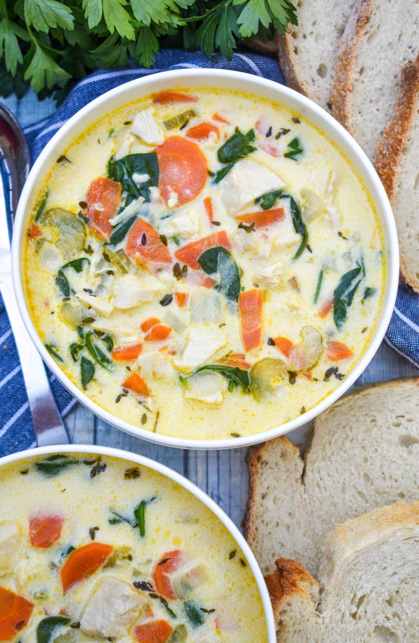 chicken florentine soup in a white bowl with fresh herbs and slices of bread on the side