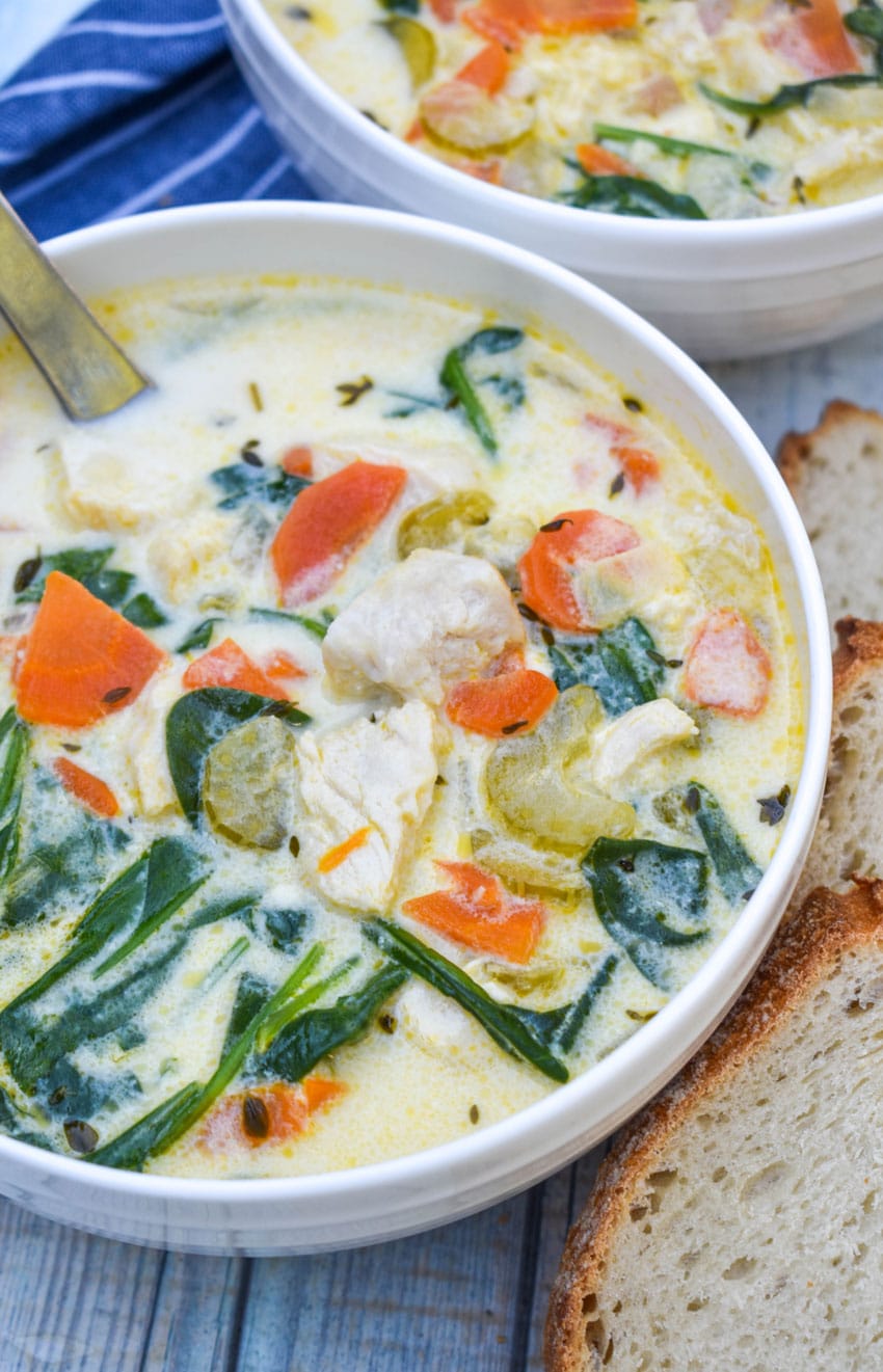 chicken florentine soup in a white bowl with fresh herbs and slices of bread on the side