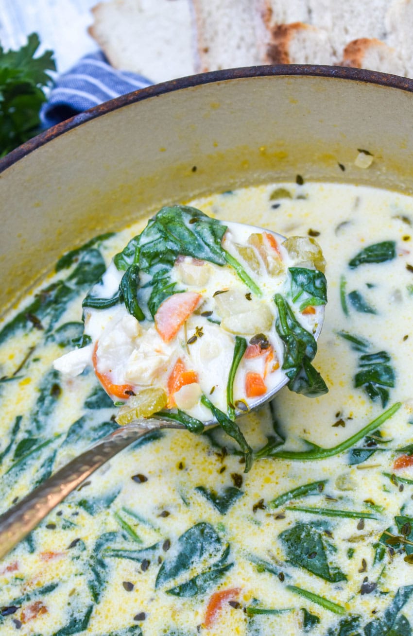 a ladle scooping chicken florentine soup out of a large red dutch oven