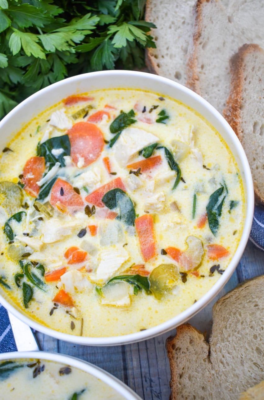 chicken florentine soup in a white bowl with fresh herbs and slices of bread on the side