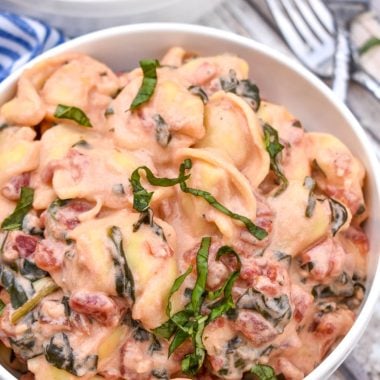 creamy tortellini with spinach and tomatoes in two white bowls with silver forks on the side
