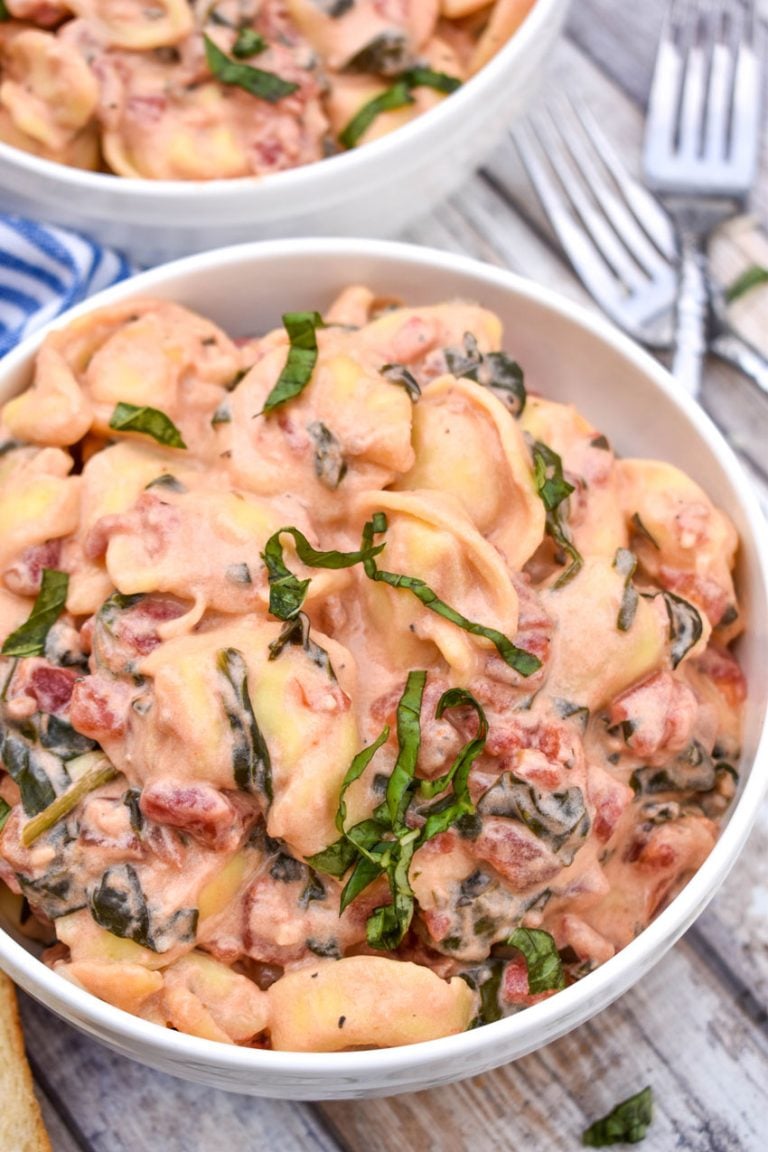 creamy tortellini with spinach and tomatoes in two white bowls with silver forks on the side