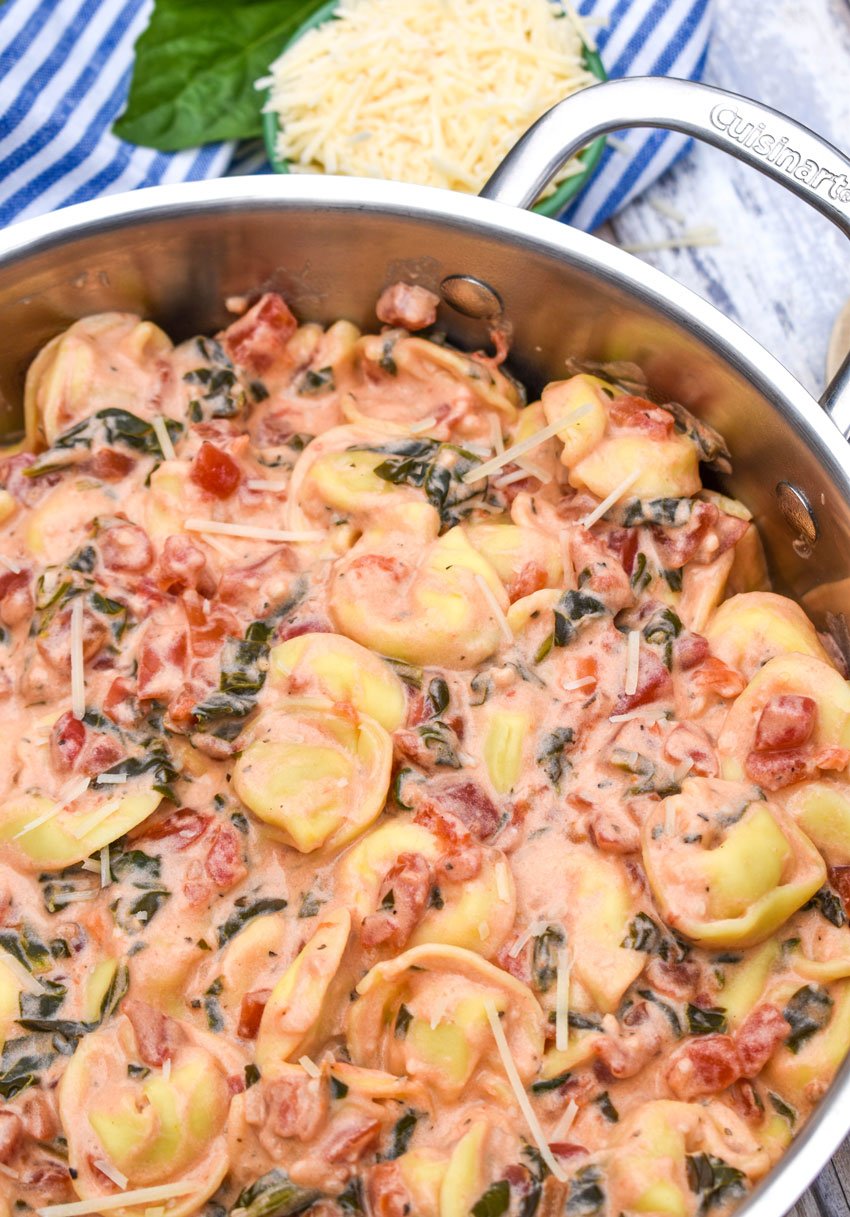 a silver skillet filled with creamy tomato tortellini with spinach