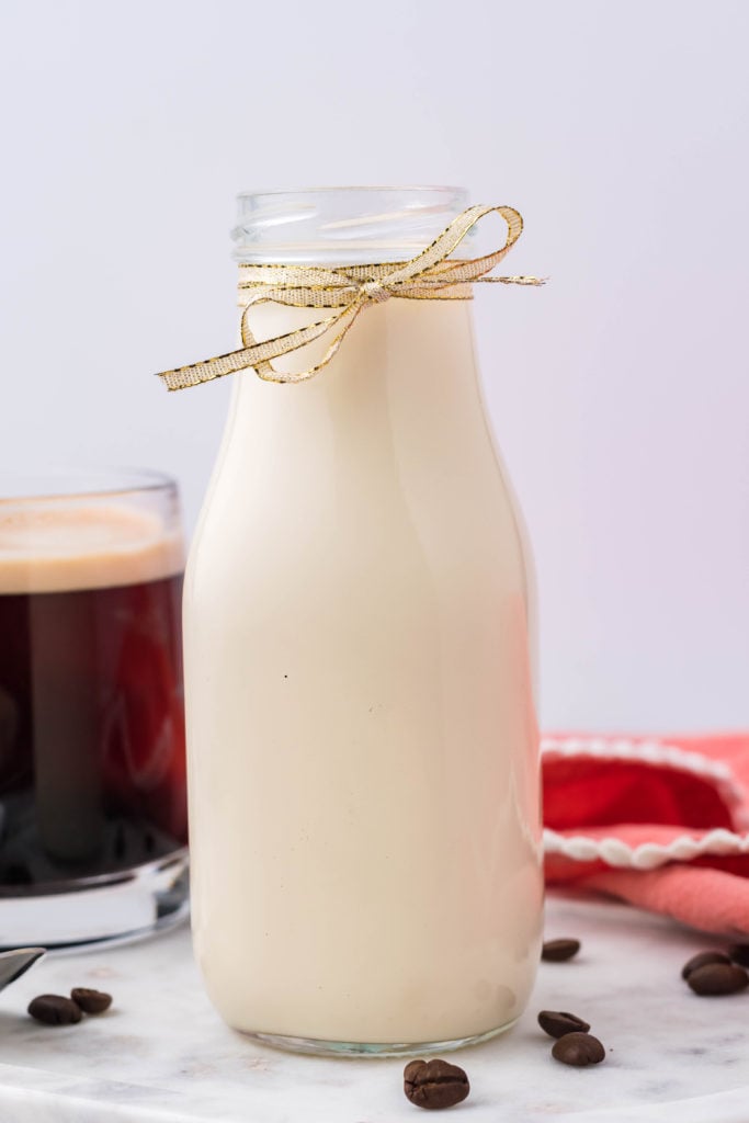 homemade French vanilla coffee creamer in a glass milk jug with a ribbon tied around it