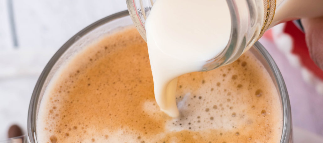homemade french vanilla coffee creamer shown being poured into a cup of black coffee in a clear glass mug