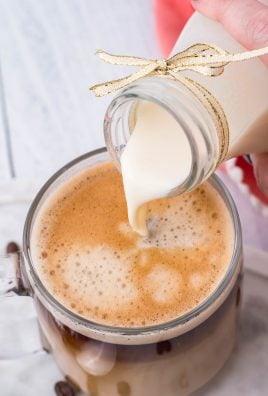 homemade french vanilla coffee creamer shown being poured into a cup of black coffee in a clear glass mug