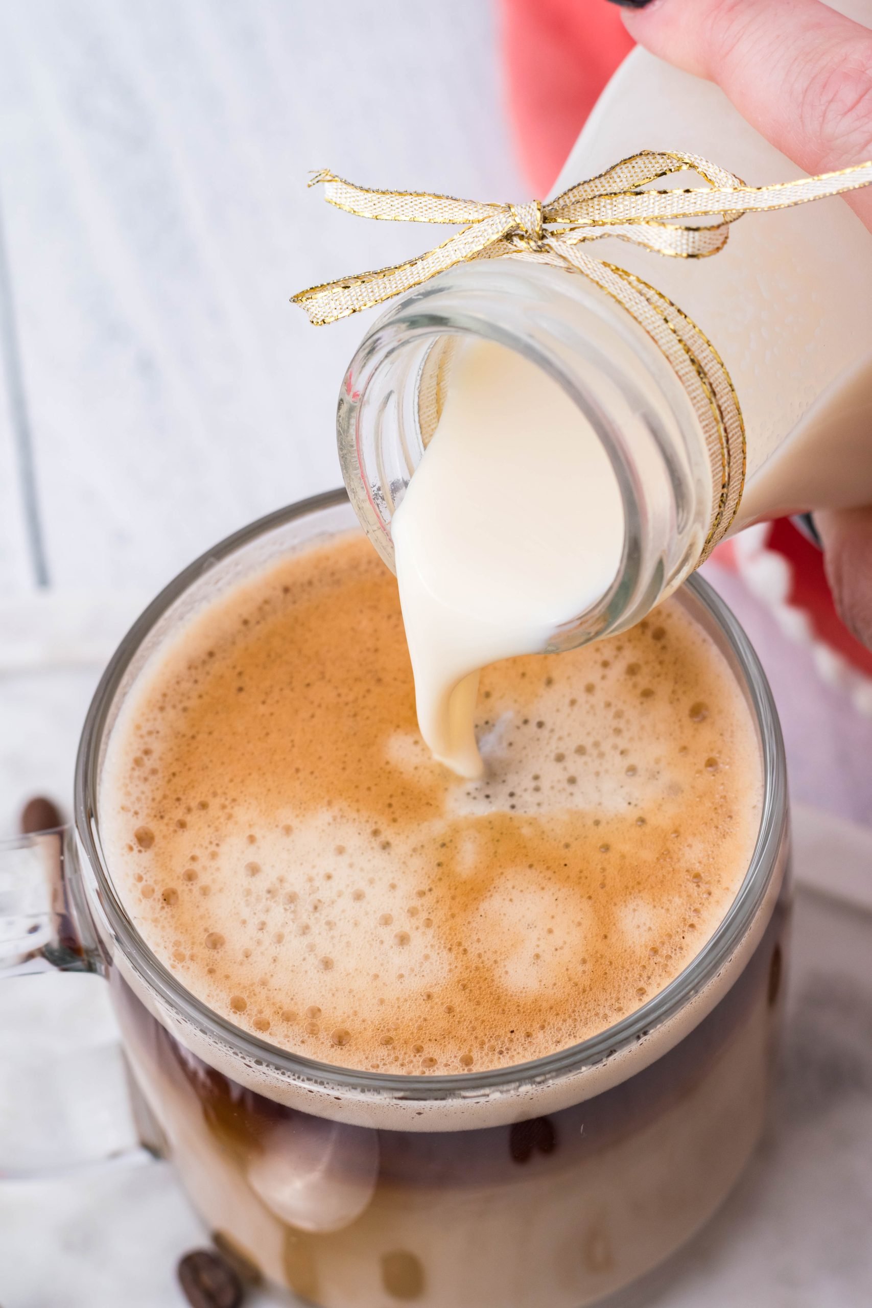 homemade french vanilla coffee creamer shown being poured into a cup of black coffee in a clear glass mug