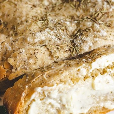 sliced crockpot rosemary & olive oil bread shown buttered and served on a white platter