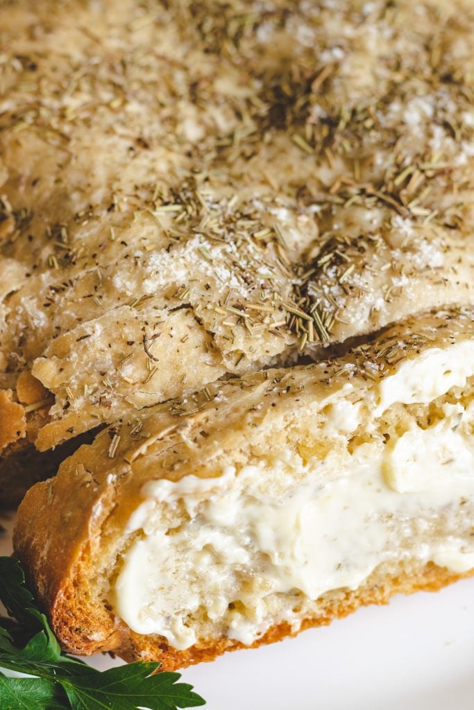 sliced crockpot rosemary & olive oil bread shown buttered and served on a white platter