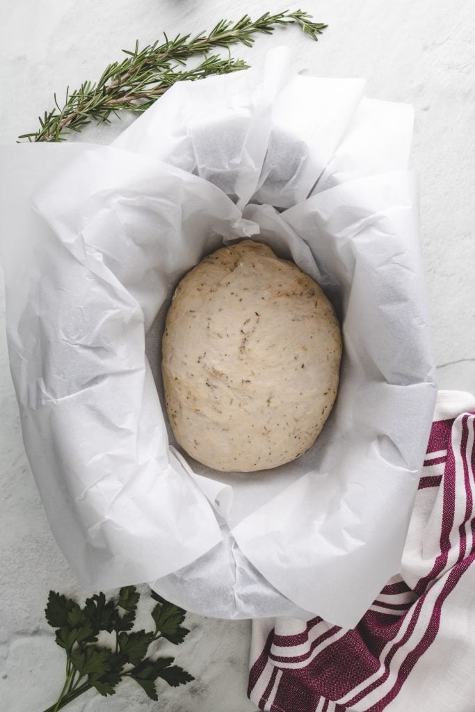 ball of crockpot rosemary & olive oil bread dough shown in the bowl of a parchment paper lined slow cooker